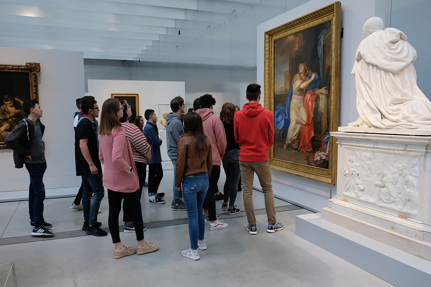 Pendant que Pierre interroge les visiteurs du Louvre avec professionnalisme, ses camarades de classe écoutent attentivement les explications de leur professeur d’histoire de l’art. 