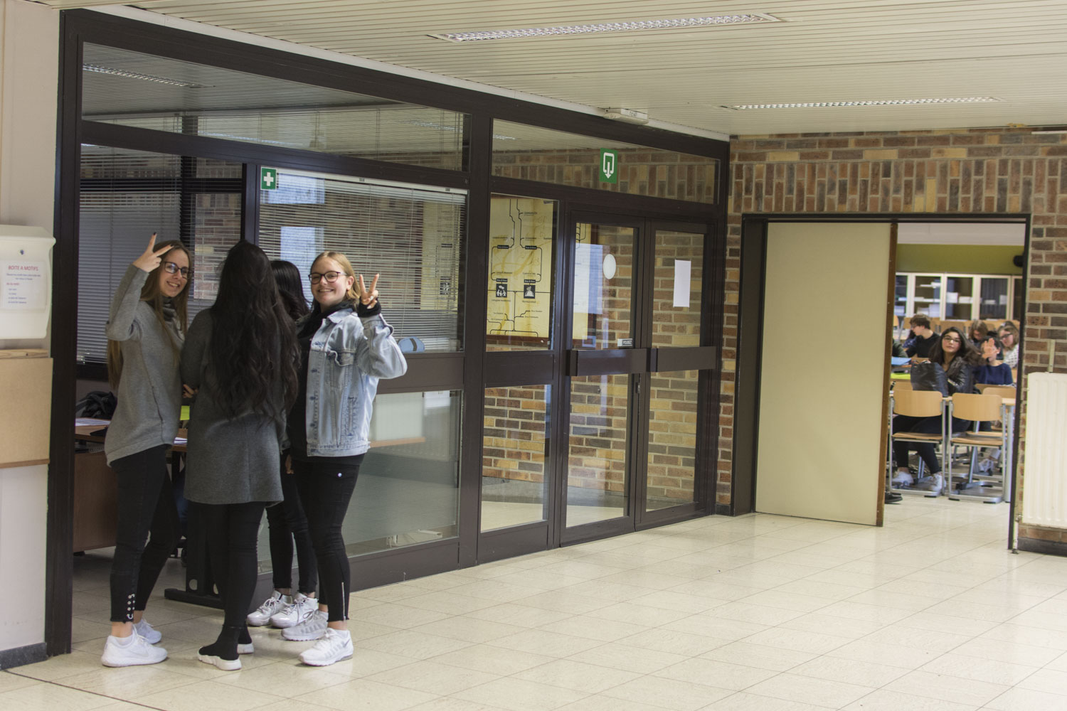Un groupe de filles aident une éducatrice à scotcher des affiches sur les panneaux d’information dans le hall d’entrée