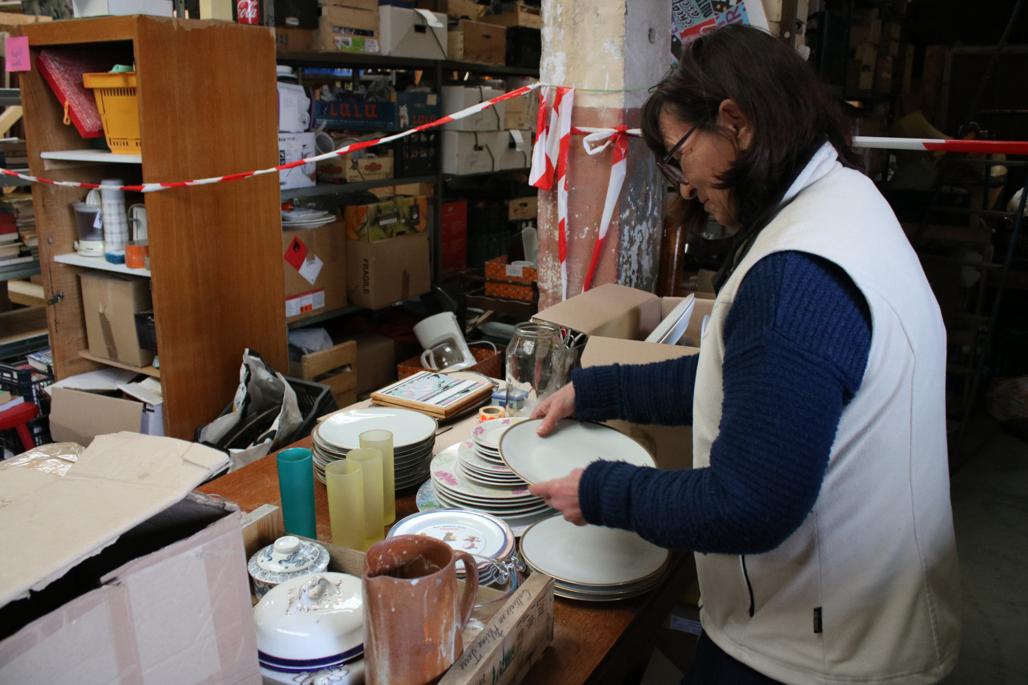 Brigitte, une bénévole, est chargée du rayon vaisselle. Elle trie des assiettes et jette celles qui sont cassées. Les autres seront mises en rayon © Anouk PASSELAC / Globe Reporters