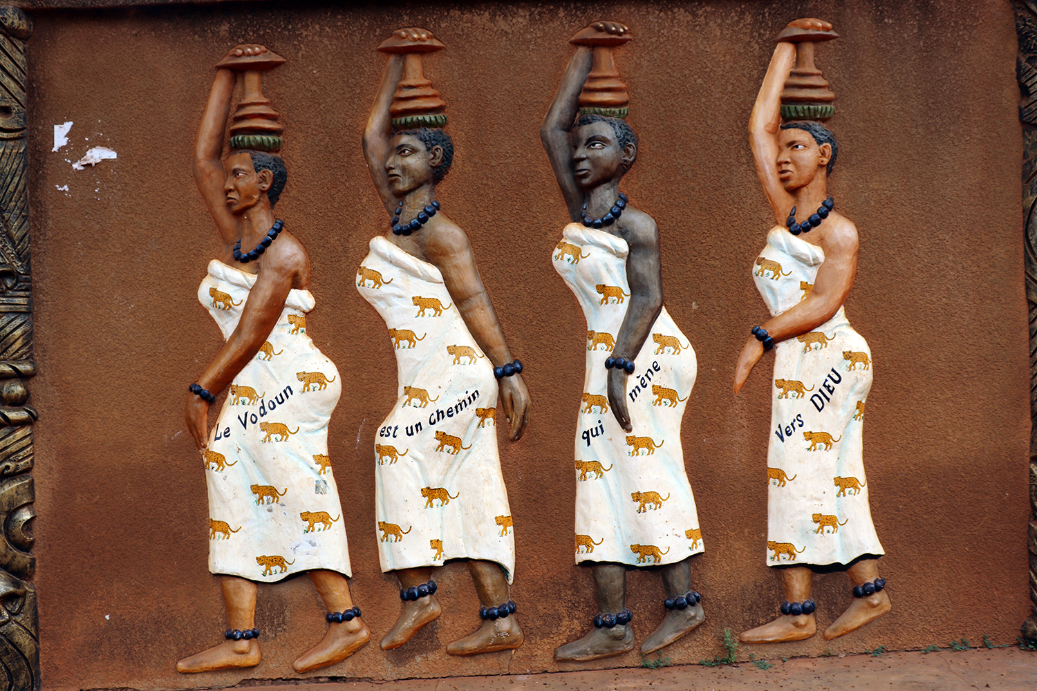 Des femmes âgées ou des filles transportent l’eau purificatrice de l’endroit où se fera la cérémonie vaudou. Le message inscrit sur leurs vêtements explique que le vaudou est un dieu unique. 