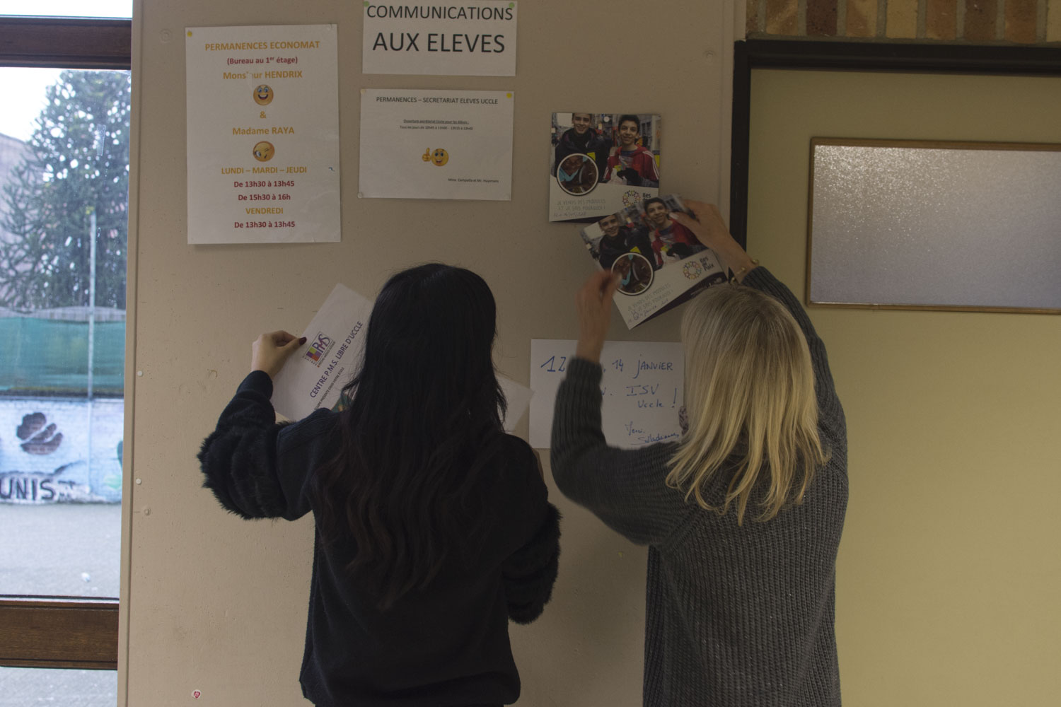 L’éducatrice (à droite) guide les élèves pour décrocher et accrocher les affiches