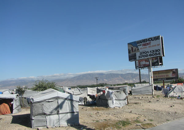 Le contraste haïtien. Au-dessus du campement de fortune de l’aéroport s’élève une publicité en anglais pour de belles maisons à louer.